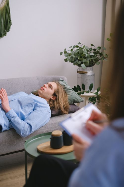 Free A person in therapy lying on a sofa with a therapist taking notes nearby. Stock Photo