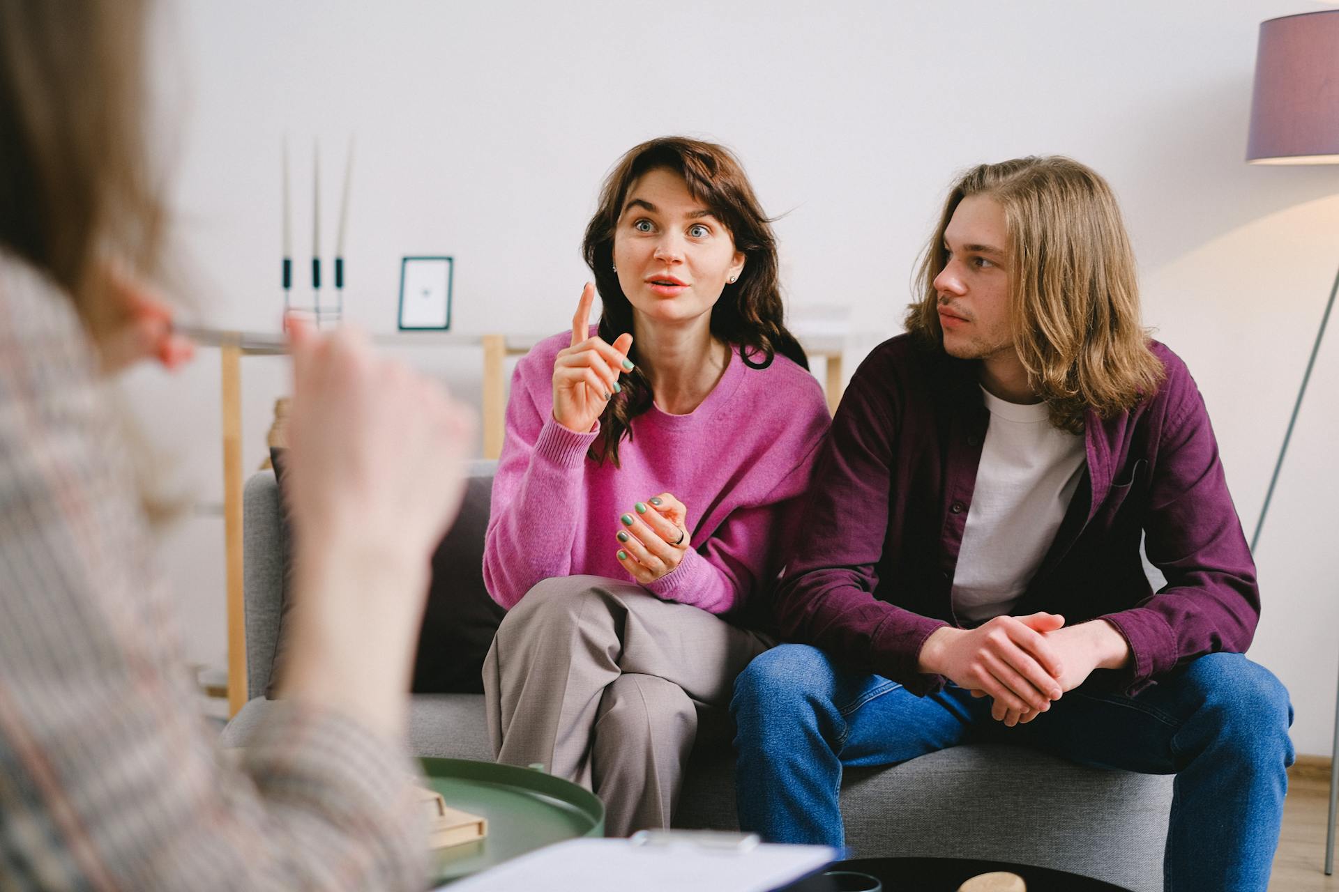 A young couple engaged in a therapy session, discussing with a therapist in an indoor setting.