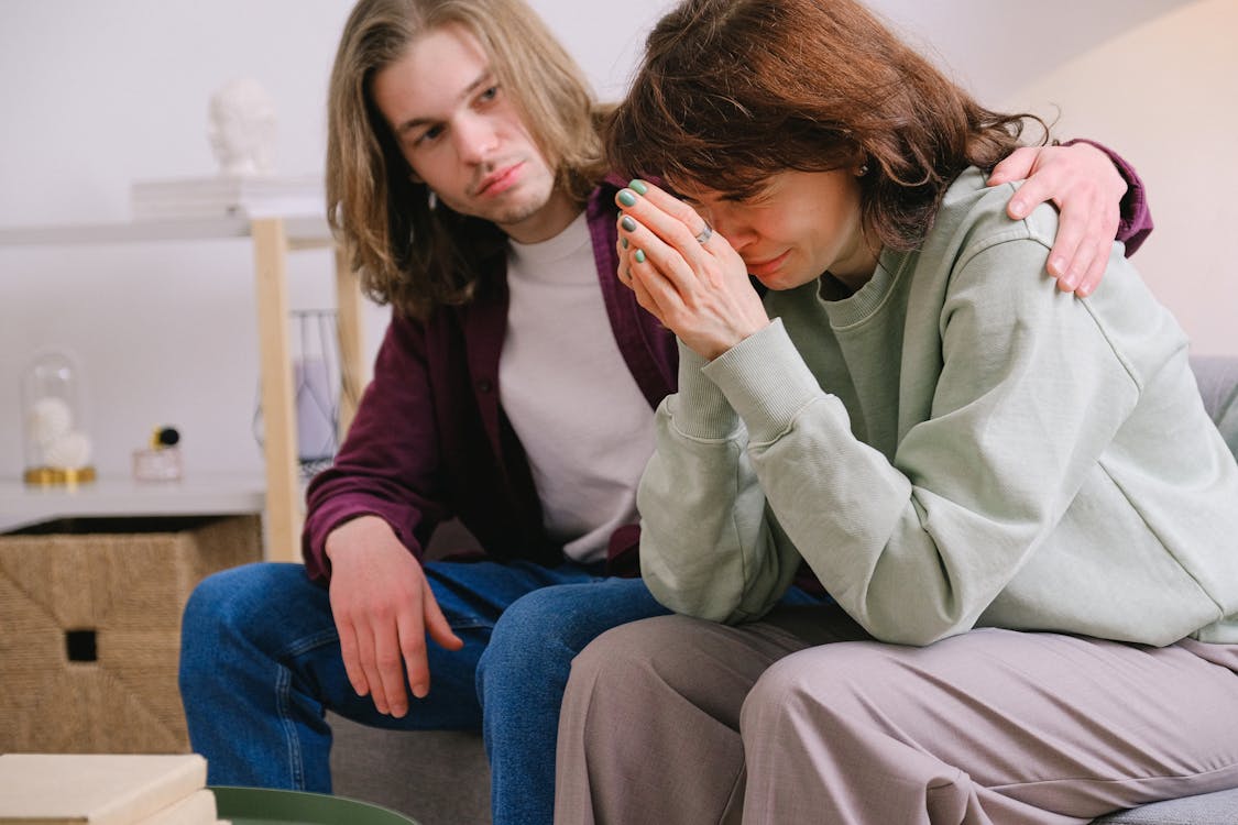Free Crop male soothing disappointed crying female in sweatshirt and gray trousers on blurred background Stock Photo