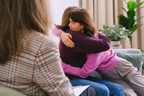 Side view of couple sitting on sofa and embracing during session with psychologist in light room in daytime