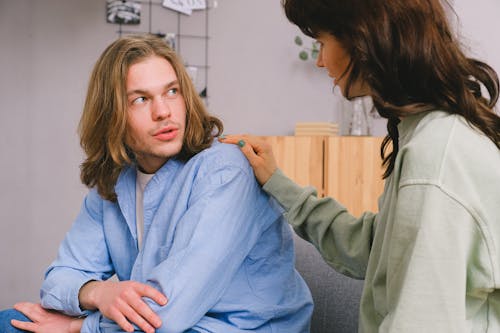 Concentrated woman talking and touching shoulder of pensive male in light room in daytime