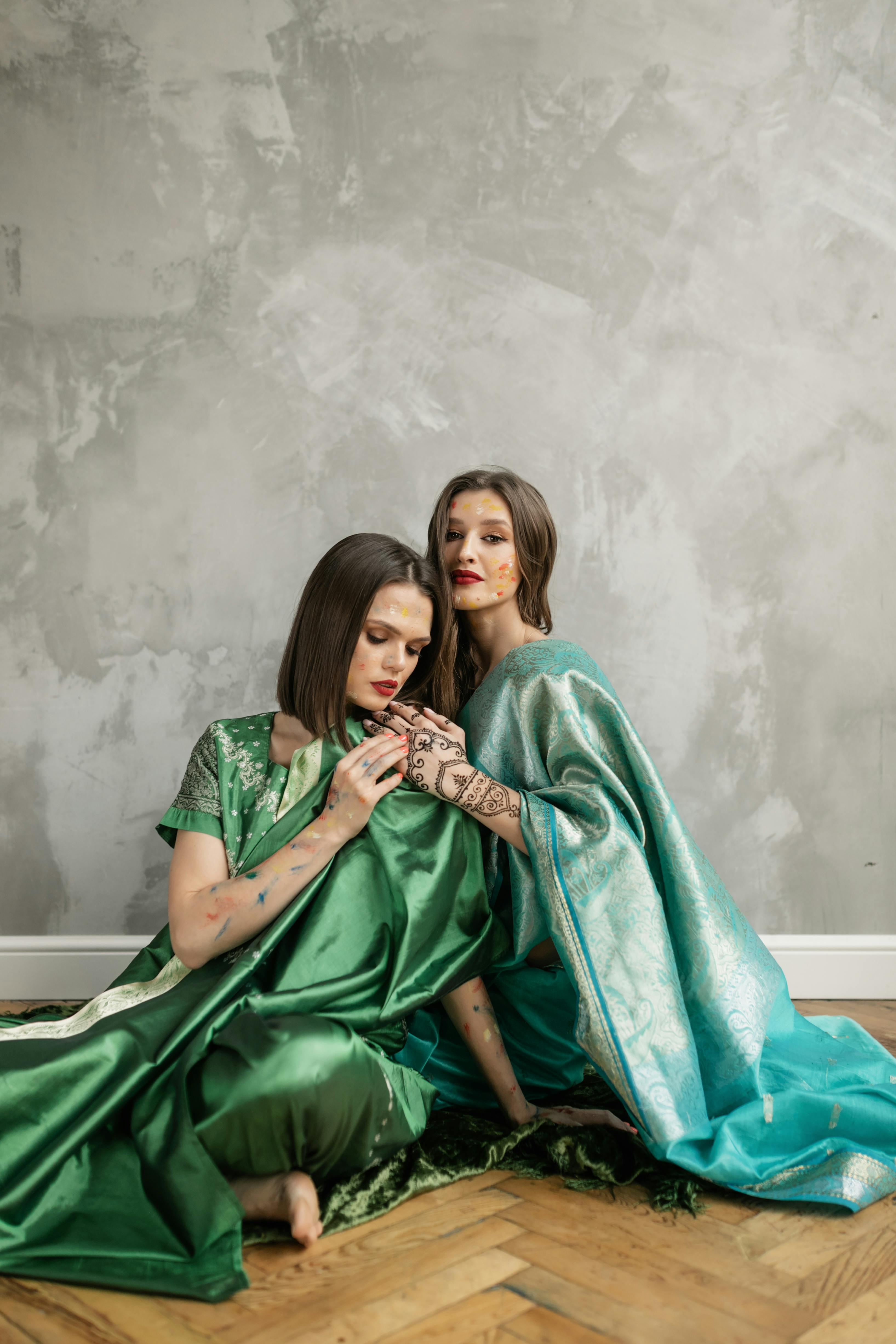 two women in green and blue robe sitting on wooden floor