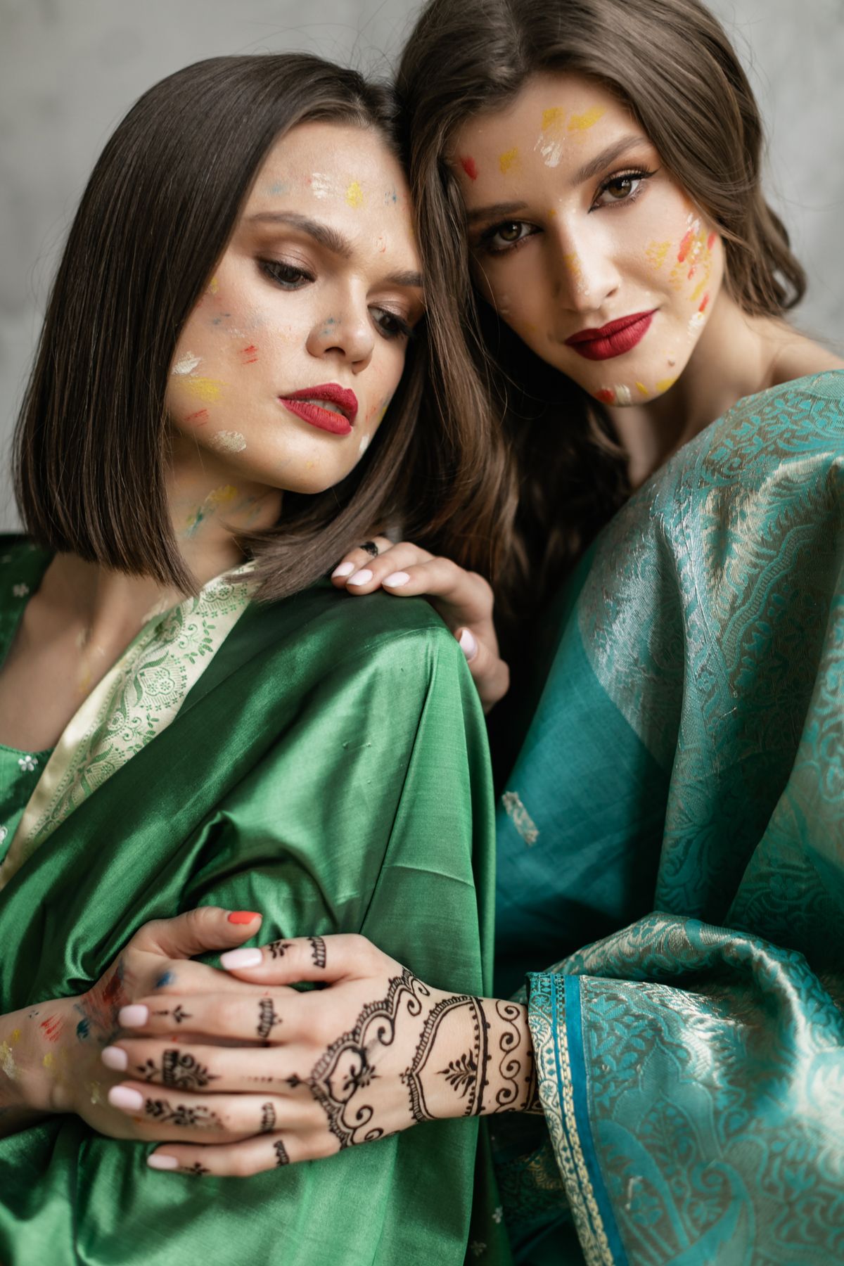 Two women in emerald and teal silk sarees with henna-adorned hands