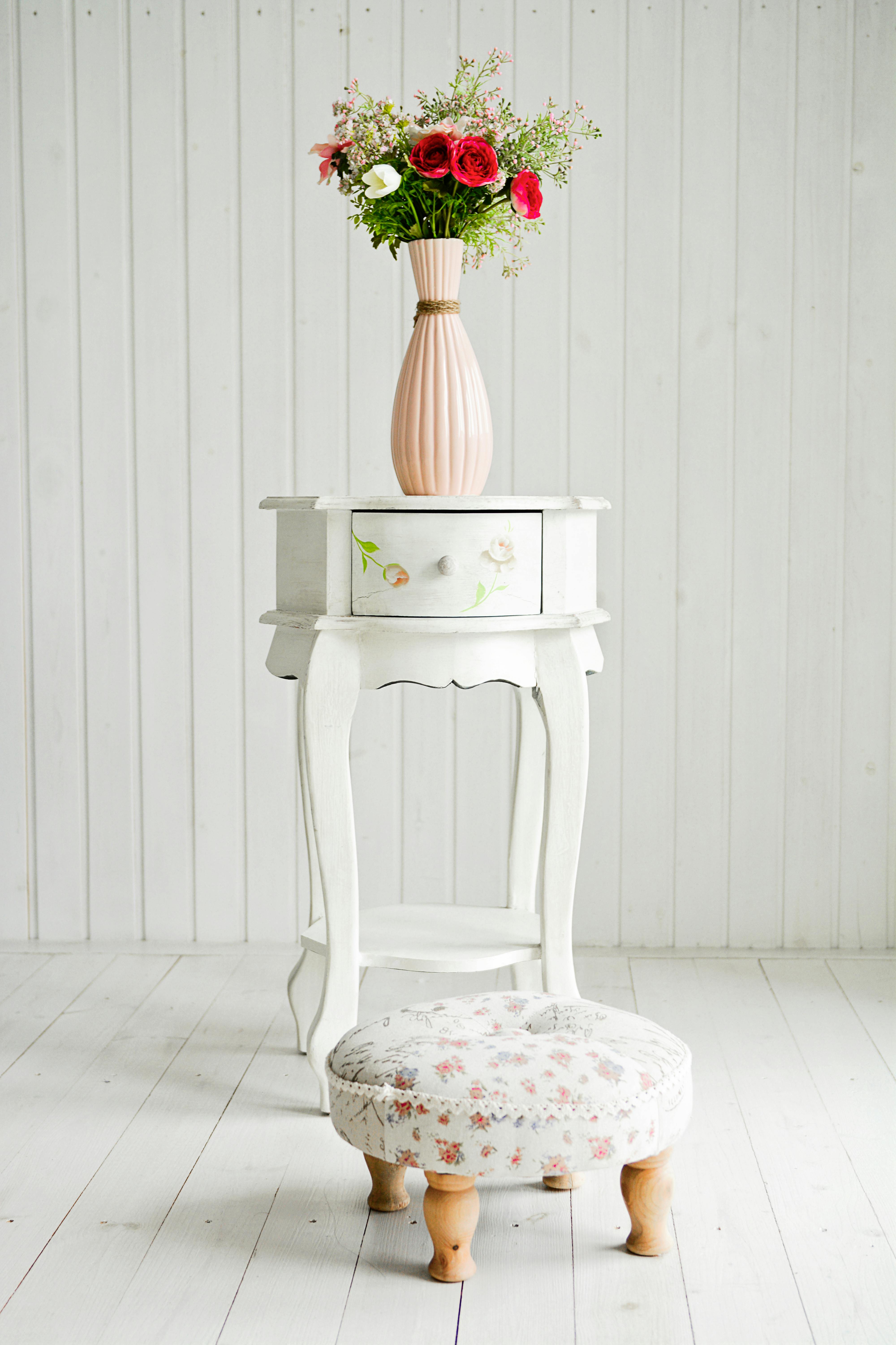 A vase with fresh flowers on an elegant vintage table and floral footstool.