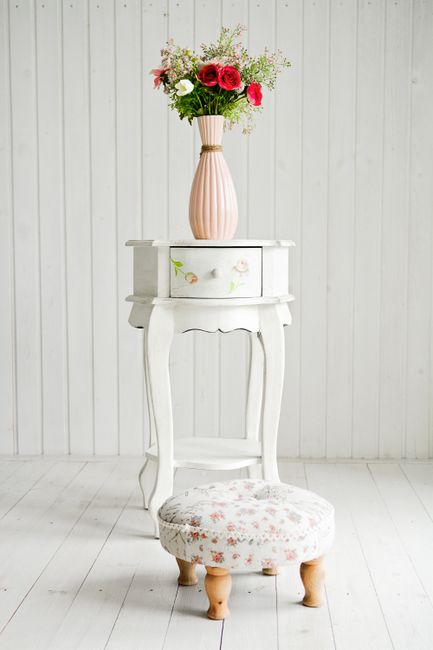 A vase with fresh flowers on an elegant vintage table and floral footstool.
