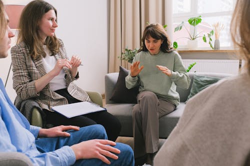 Women in casual clothes sitting on sofa and speaking during group psychotherapy session in cozy office