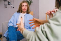 Unrecognizable therapist talking to male patient and anonymous partner during psychotherapy session in light office