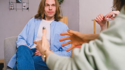 Unrecognizable therapist talking to male patient and anonymous partner during psychotherapy session in light office
