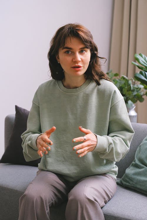 Brown haired female in casual clothes looking away and gesticulating while telling own problems sitting on sofa