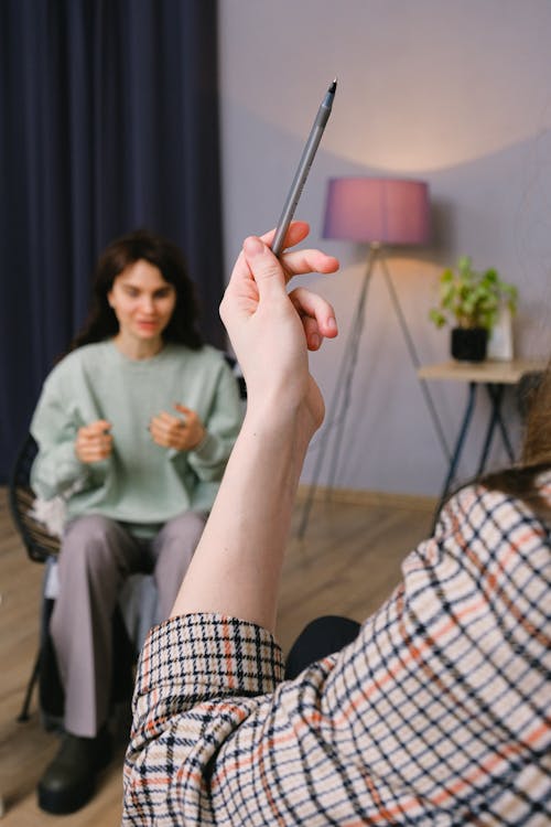 Crop unrecognizable therapist showing pen to young female patient talking about problems during psychotherapy session in modern office