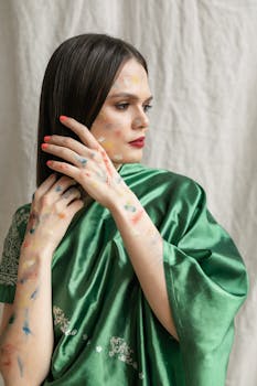 Asian woman in traditional green sari adorned with vibrant Holi festival colors.