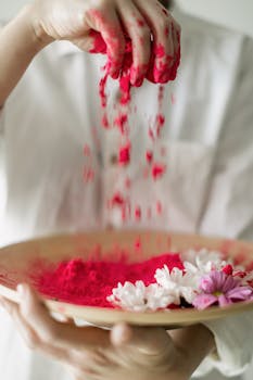 Hand gently releasing red Holi powder over flowers, celebrating the festival of colors.