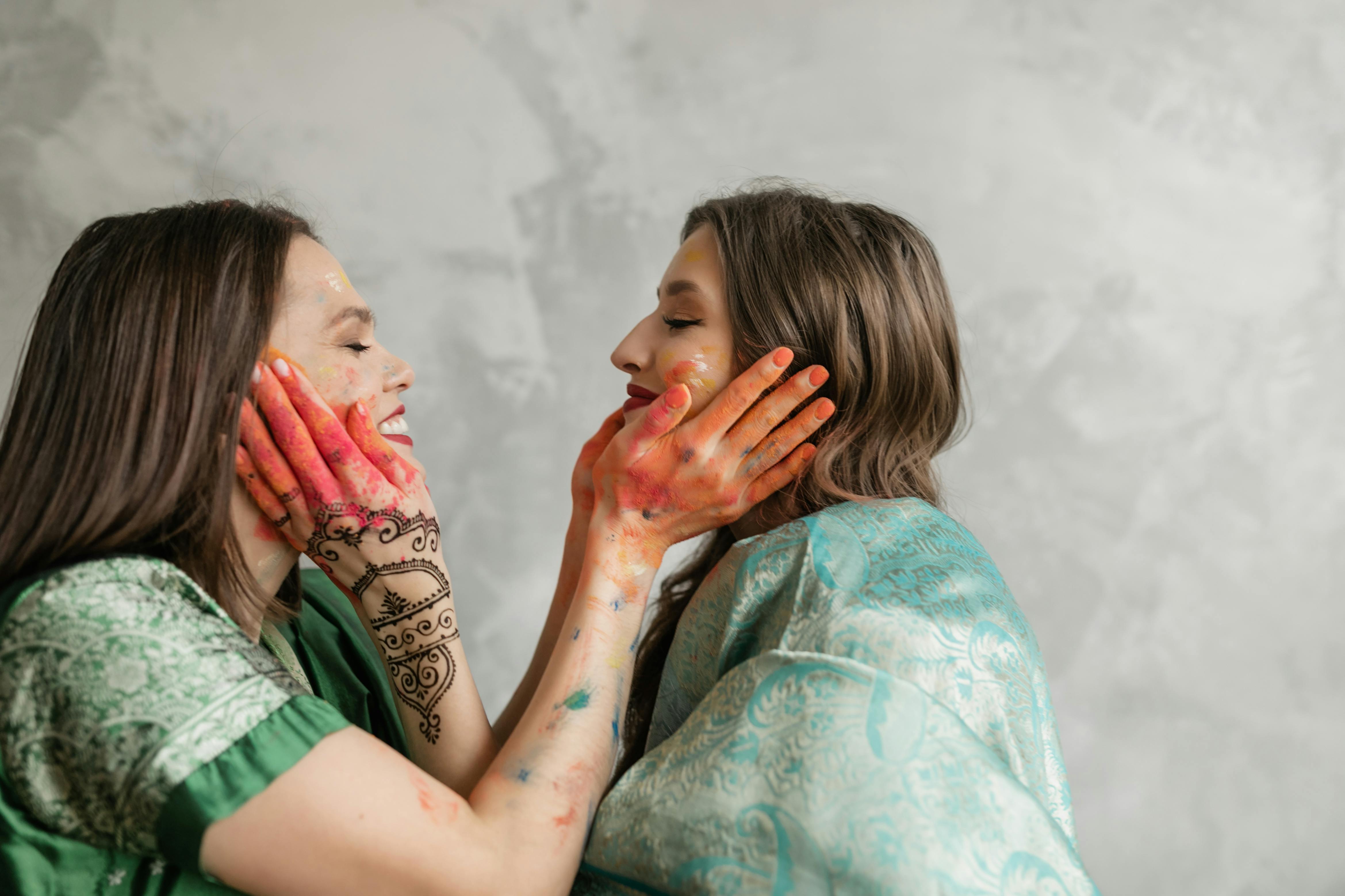 Two adult women sharing a joyful moment with colorful painted hands, celebrating together inside.