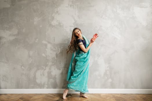 A graceful Indian woman in a traditional saree celebrates Holi indoors with vibrant colors.