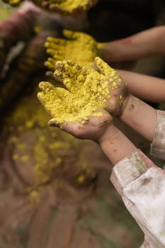 Close-up of children's hands with vibrant yellow Holi powder, capturing festive spirit.