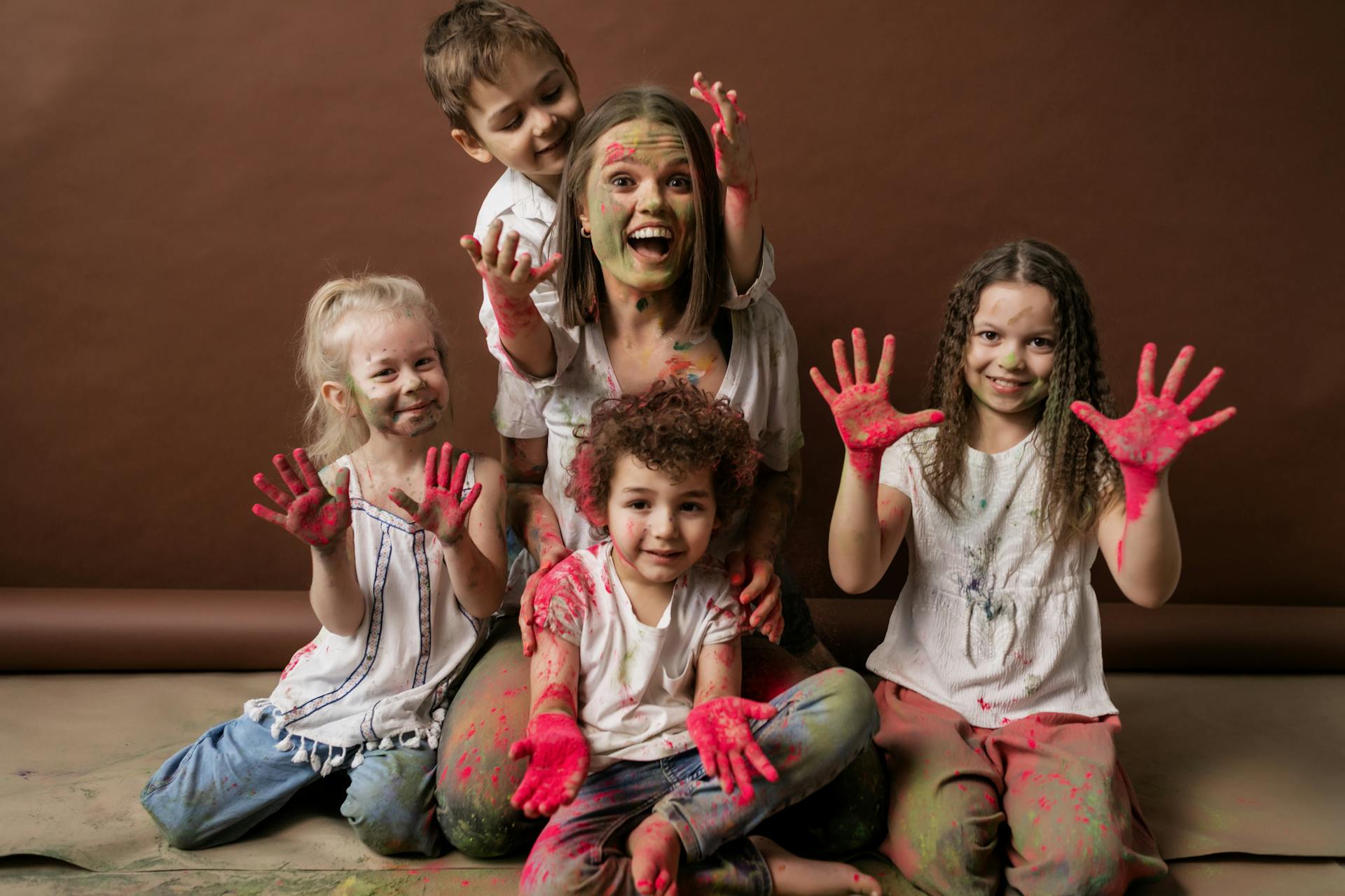 A happy group of children and woman covered in colorful powder, all smiles and joy.