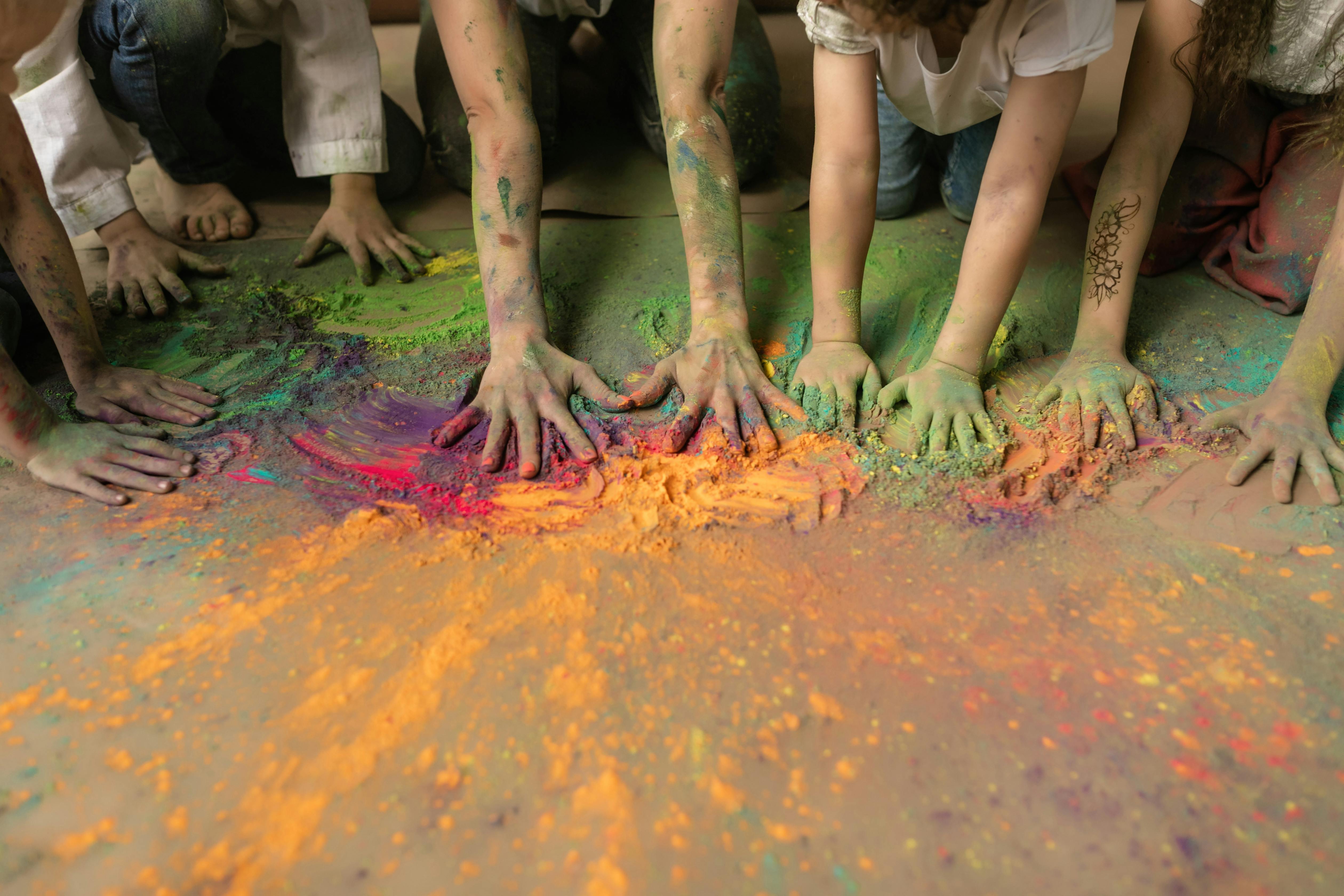 Children's hands mixing bright colored powders on a surface, showcasing creativity and play.