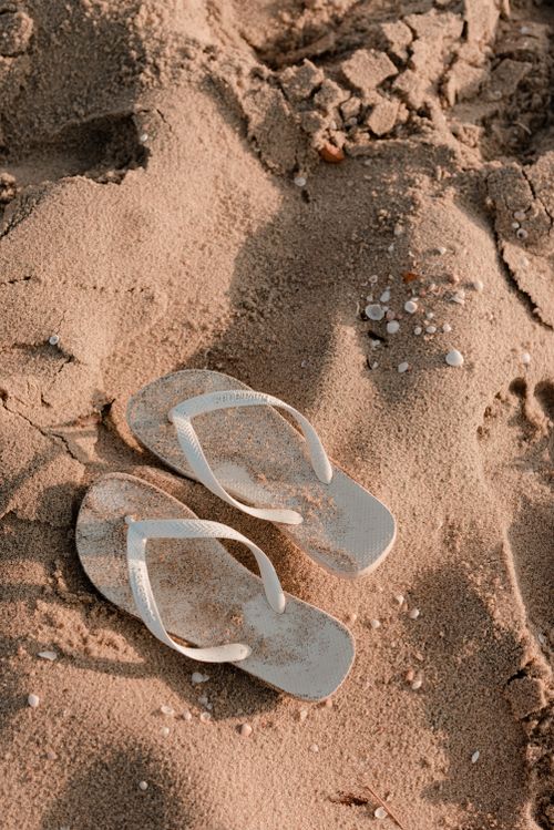 Free Pair of white flip flops on sand symbolizes relaxation and summertime beach vibes. Stock Photo