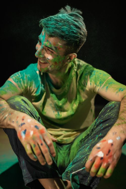 Free A cheerful young man sits covered in colorful Holi powder, capturing the joyful festivities. Stock Photo