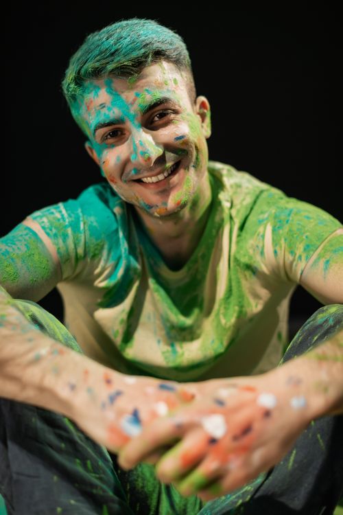 Free Smiling man covered in vibrant Holi colors on a black background. Stock Photo
