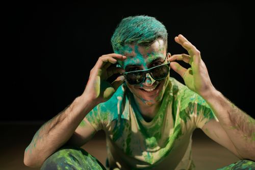 Free Happy man with sunglasses enjoying Holi festival covered in vibrant powder colors. Stock Photo