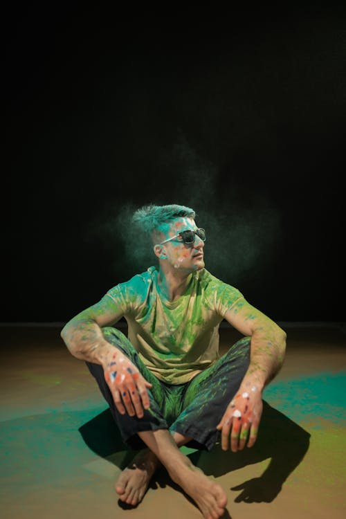 A Man with Holi Powder Wearing Sunglasses Sitting on Floor