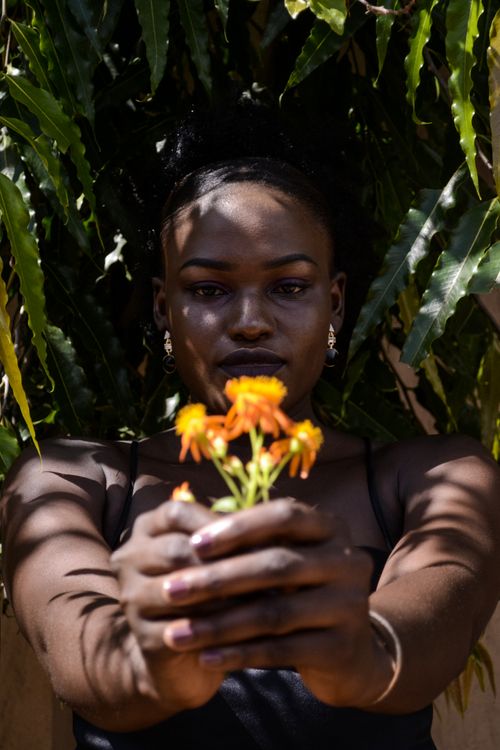 Free Artistic portrait of a woman holding yellow flowers in front of green foliage, Kampala. Stock Photo