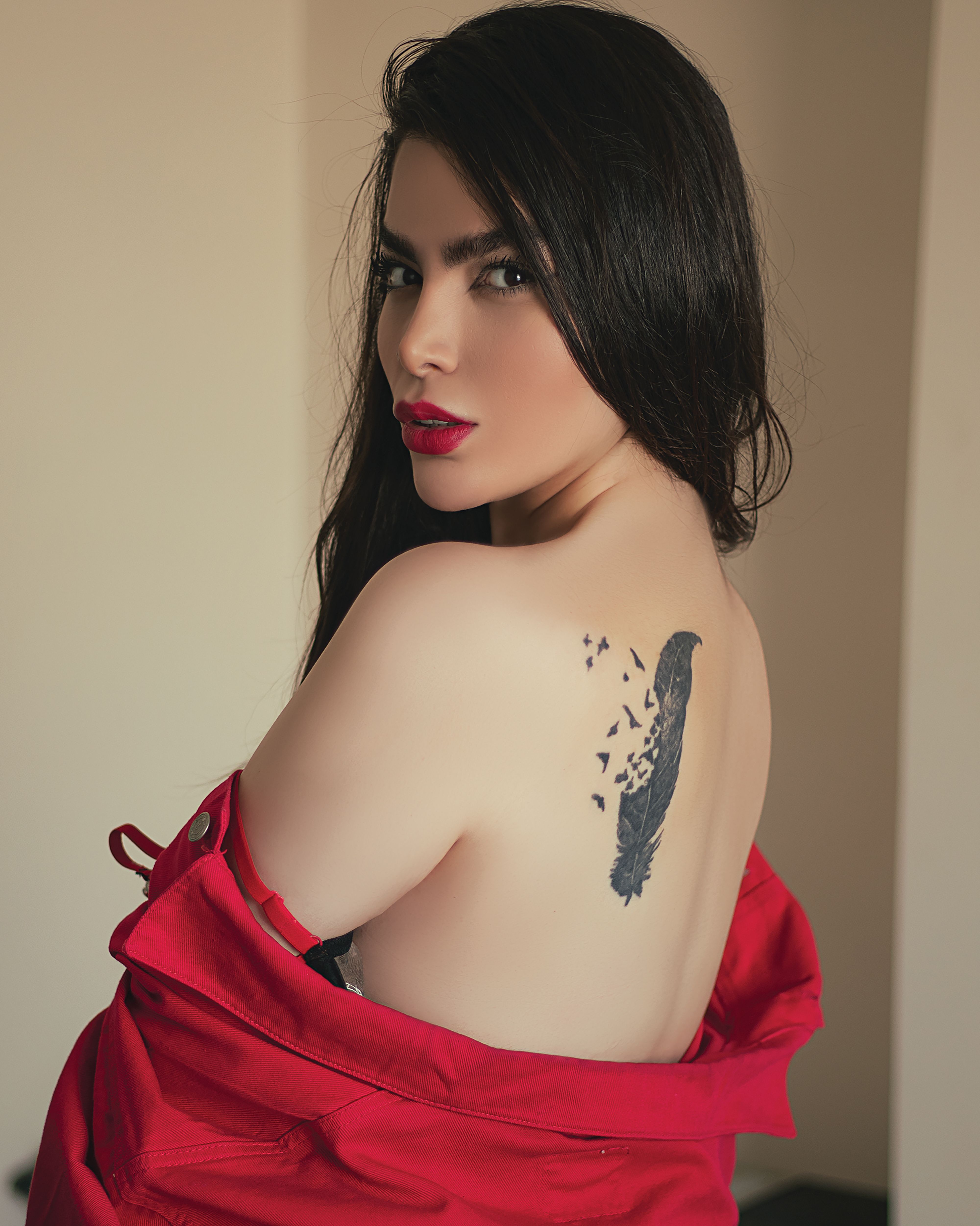 Stylish woman in red posing indoors, showcasing a unique back tattoo with artistic flair.