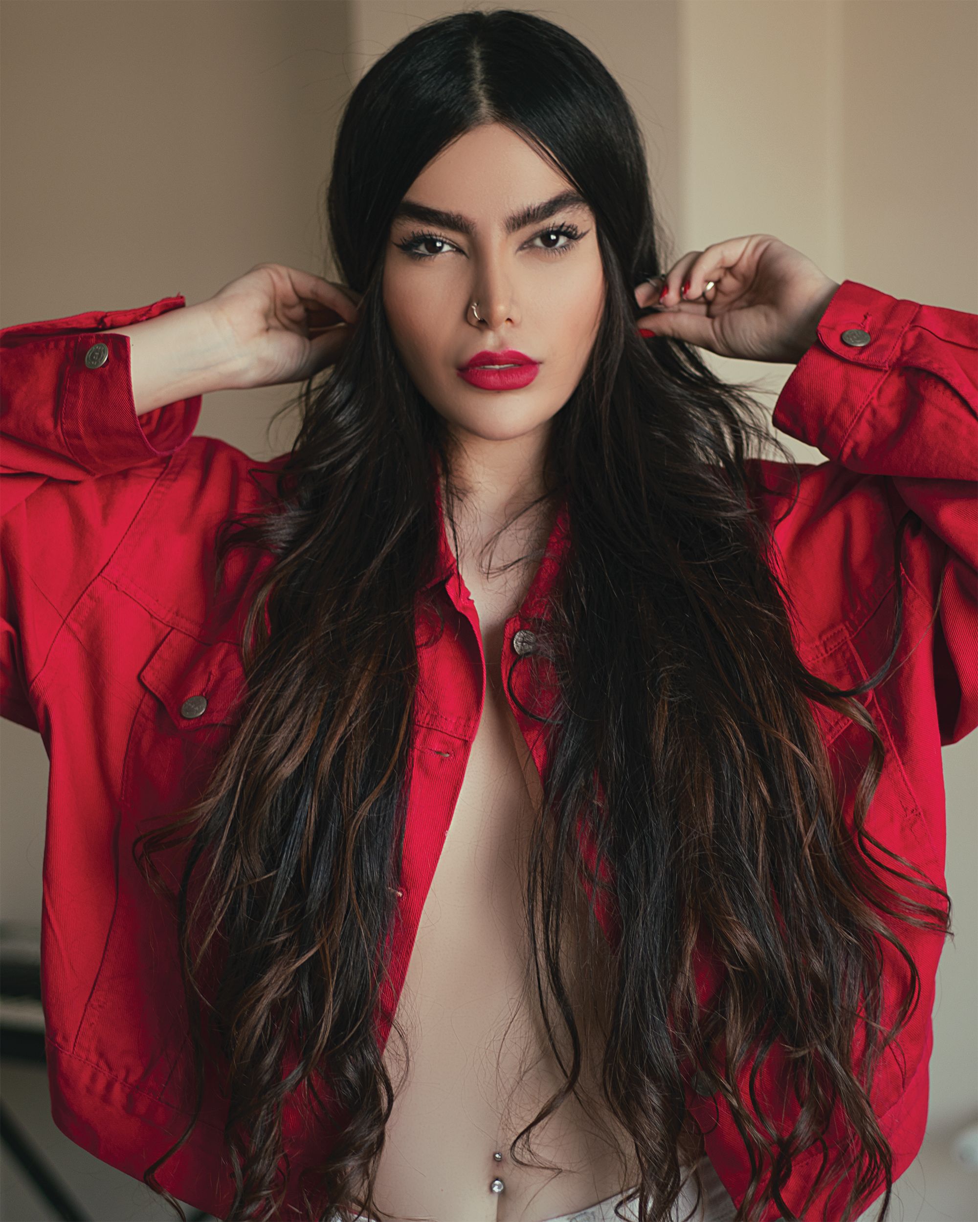 Stylish woman with red lips in a red jacket posing indoors, embodying elegance and confidence.