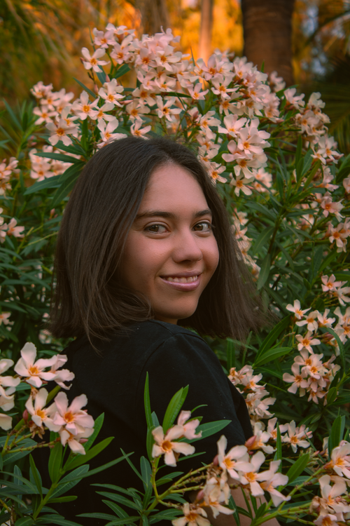 Free Portrait of a young woman smiling in a garden surrounded by blooming flowers. Stock Photo