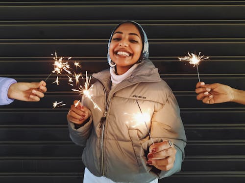 Joyful black woman with sparklers near friends