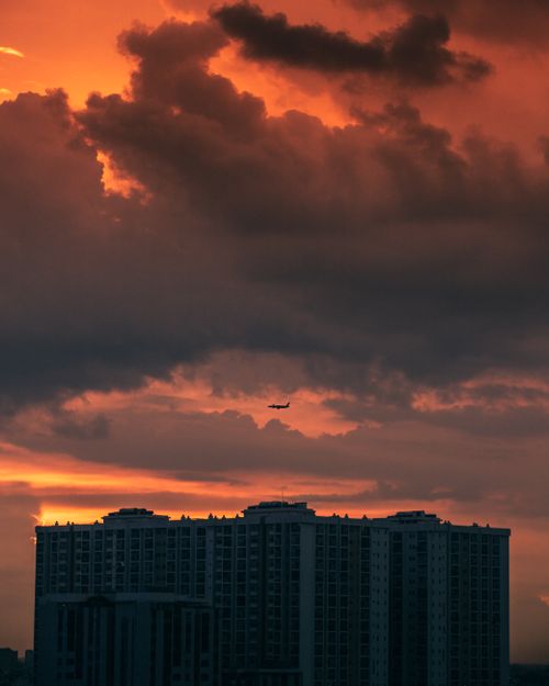 Free Vibrant sunset with dramatic clouds over Ho Chi Minh City skyline and a distant airplane. Stock Photo