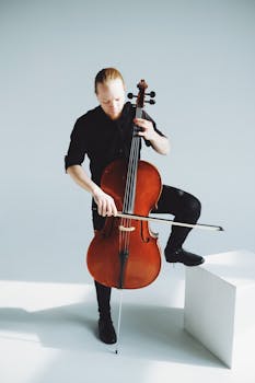 A musician engrossed in playing the cello, captured in a bright and minimalist setting.