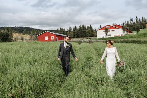 Man in Black Suit Walking on Green Grass Field  Beside Woman in White Dress at Wedding Day