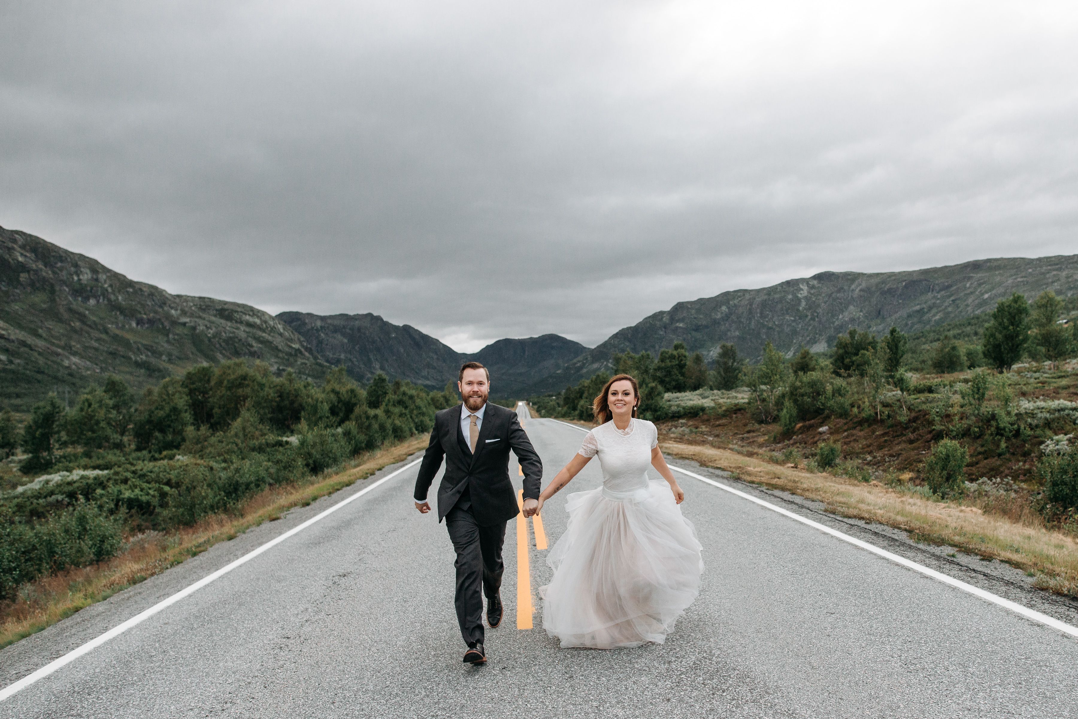 Newlywed couple joyfully running along a scenic mountain road.
