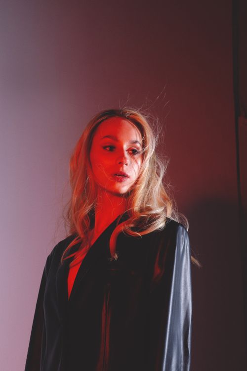 Free Emotionless young woman in leather black jacket looking away in bright studio with red neon lights Stock Photo