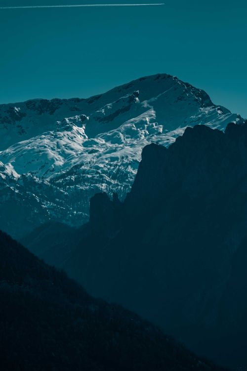 Free High steep mountain range covered with white snow located near silhouettes of rock against cloudless blue sky on winter day in nature Stock Photo