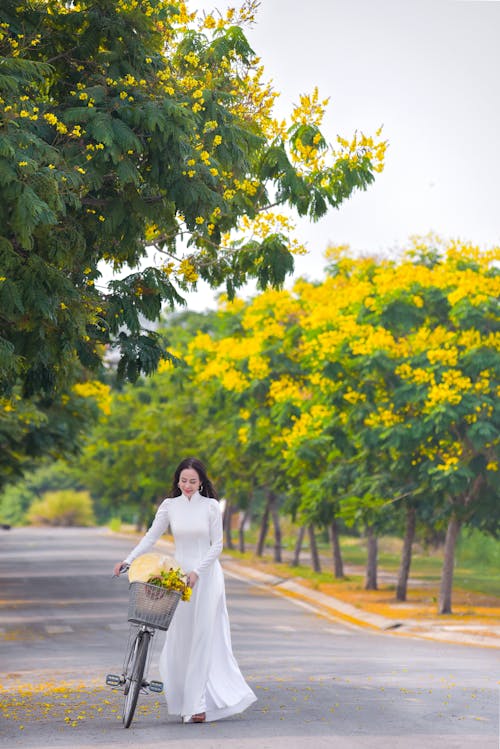 A Woman in White Dress Walking on the Road with Bicycle