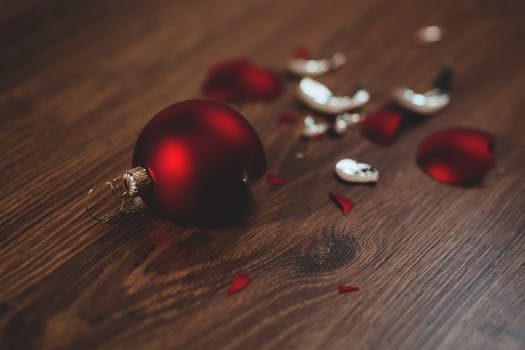 A close-up image of a broken red Christmas ornament on a wooden floor.