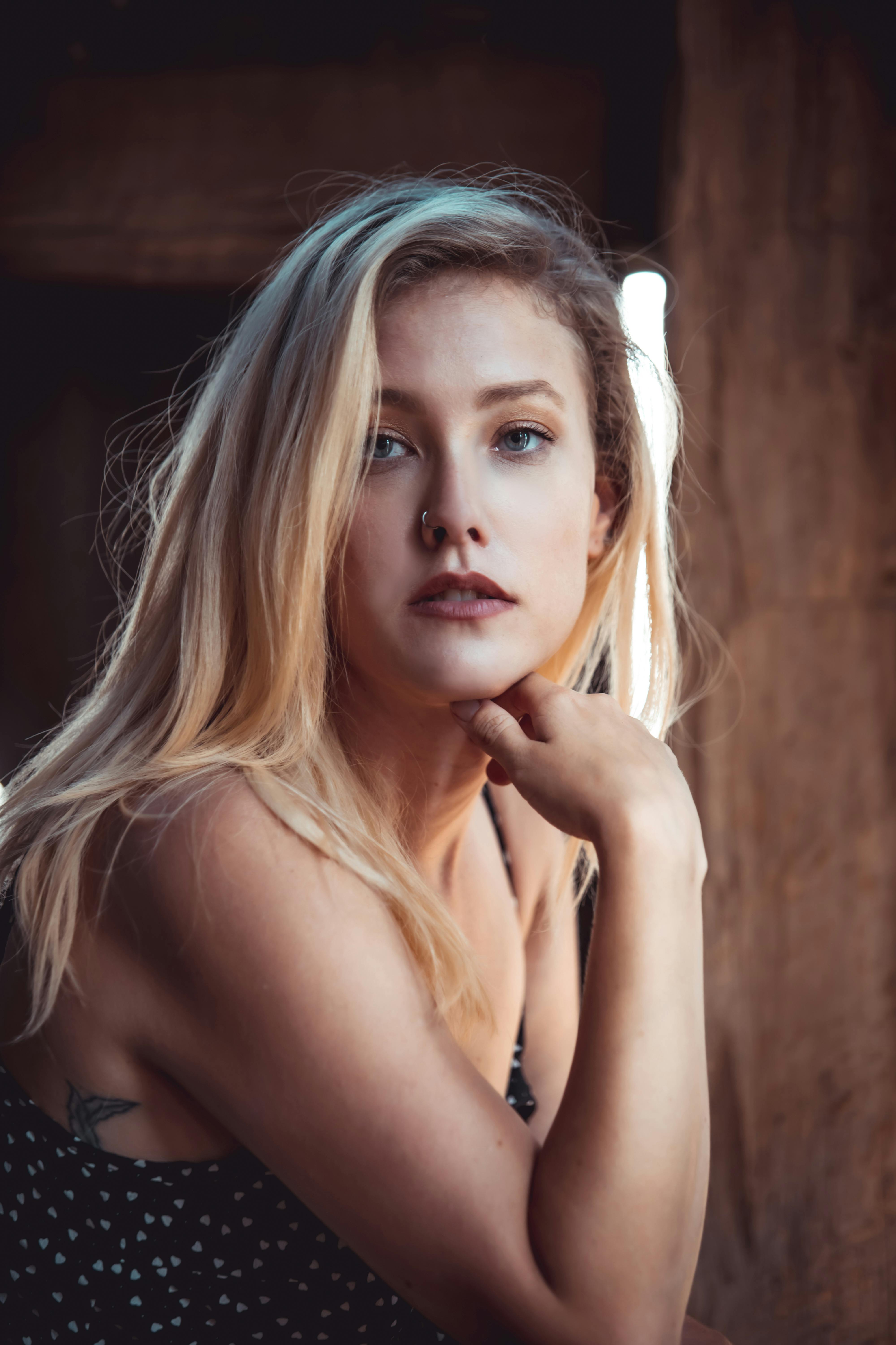 A beautiful blonde woman posing indoors with a thoughtful expression under warm natural light.