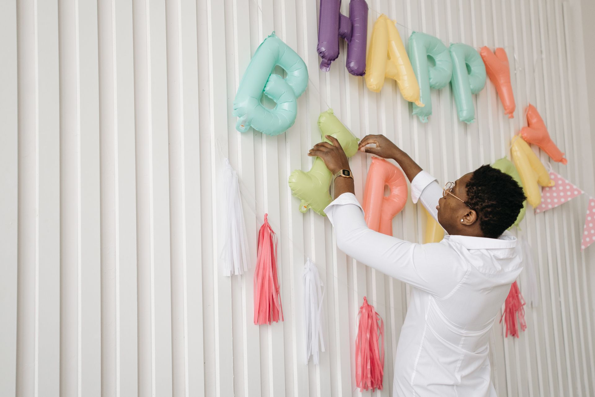 A man sets up colorful balloon decorations for a birthday celebration indoors.