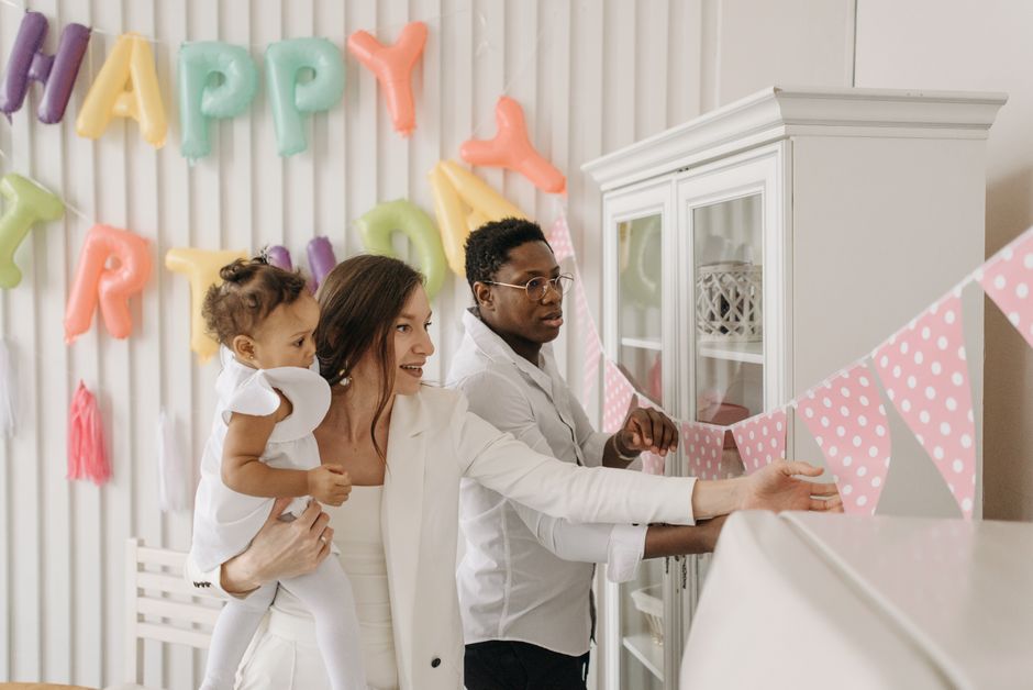 A family decorates a room with colorful pennant banners for a birthday celebration.