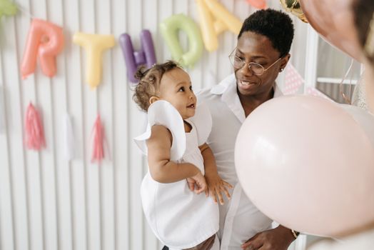 A joyful father and daughter celebrating a birthday with colorful balloons indoors.