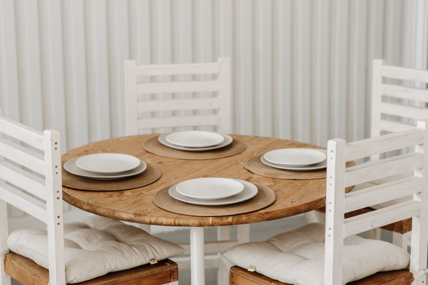 A round table laid with plain stoneware plates, waiting for the people who will find out whether they chip.