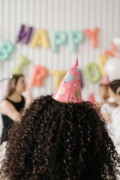 Back view of child at a vibrant birthday party with balloons and party hat.