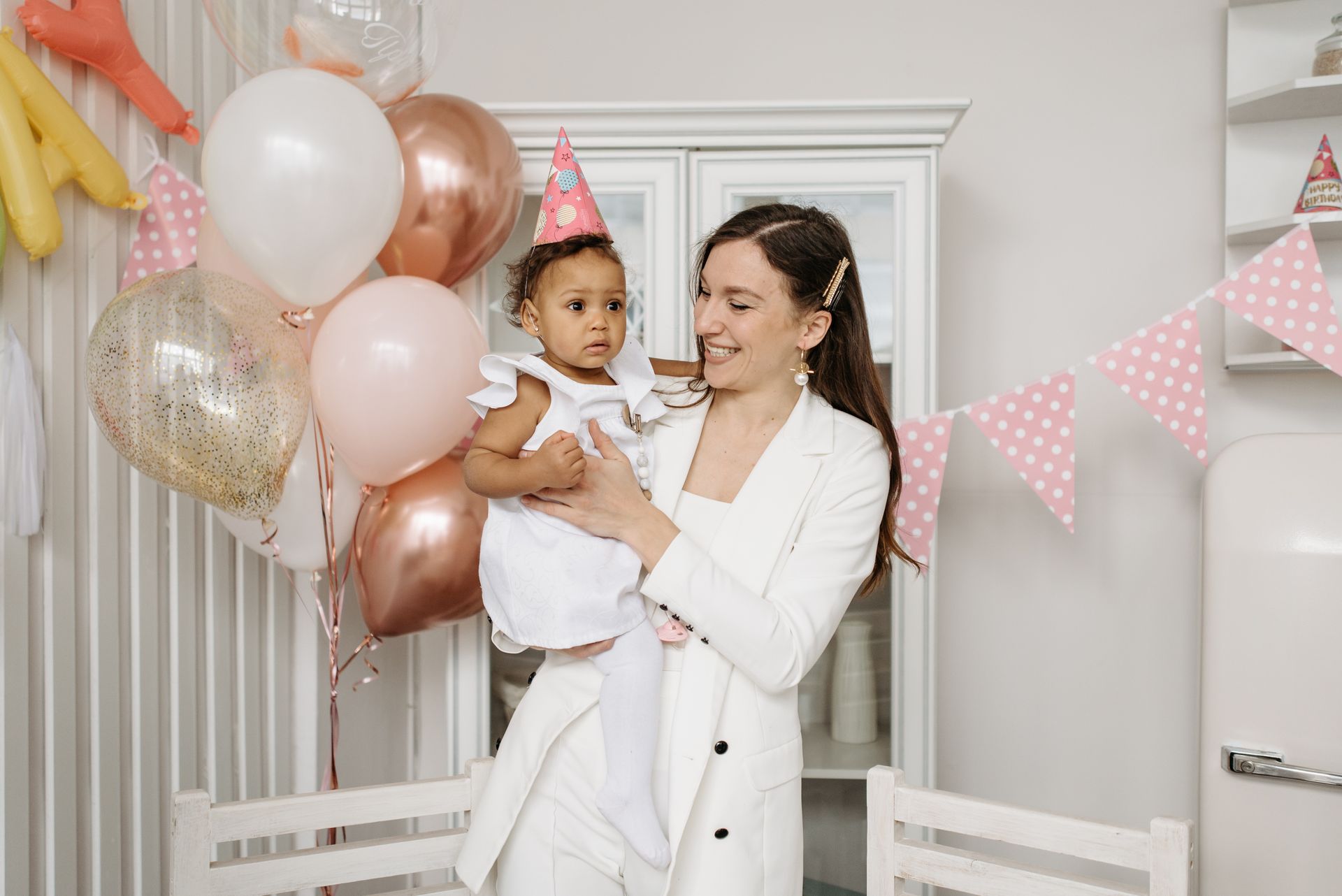 Mother and daughter enjoying a birthday celebration with balloons and party hats.