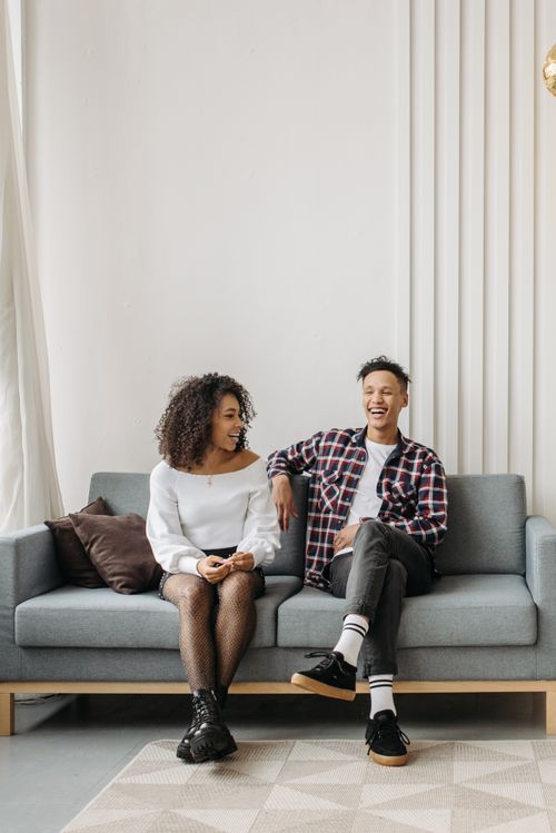 Free Two friends happily laughing together while seated on a comfortable sofa indoors. Stock Photo