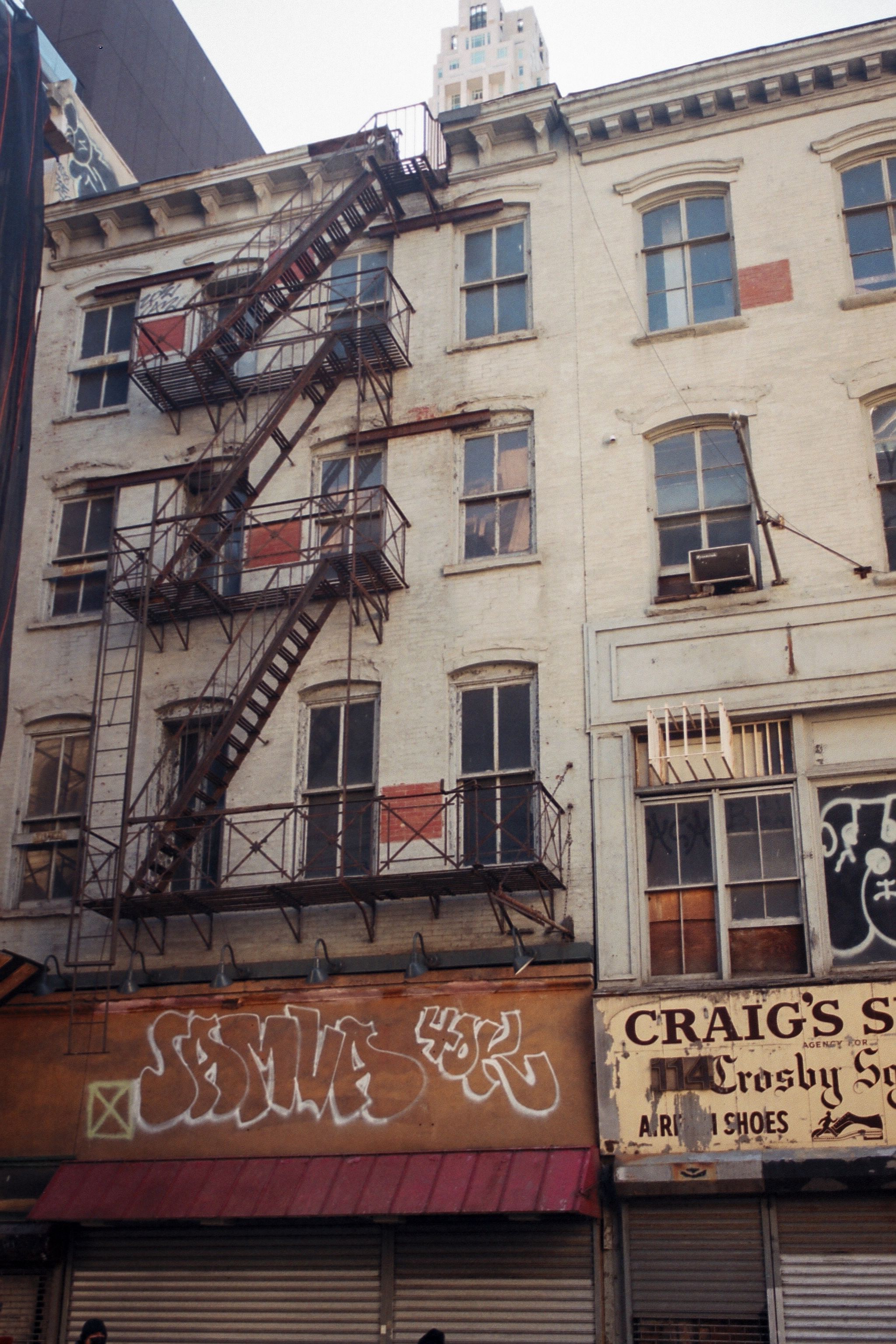 A vintage building facade featuring graffiti, fire escape, and city signs in urban downtown.