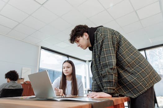 Two young professionals collaborating over a laptop in a bright modern office environment.