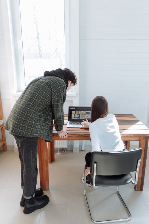 Free Two adults engaged in teamwork around a laptop in a sunlit office space. Stock Photo